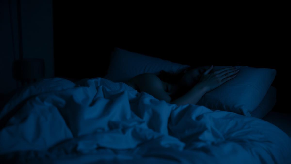 Person asleep in bed in a dark bedroom lit by faint blue night light